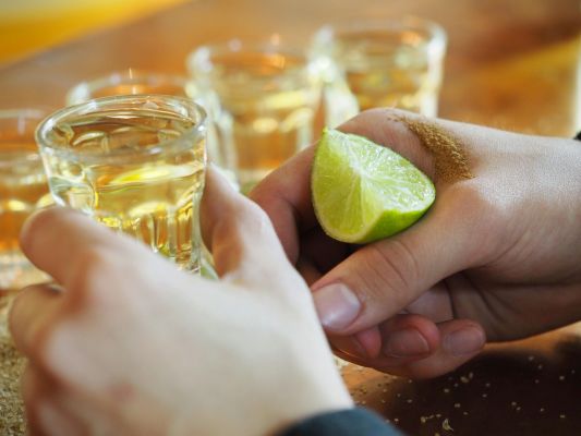 Hands holding tequila shots with lime wedge and salt, capturing essence of a classic drink.